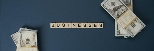 Letter tiles spelling BUSINESSES between two piles of banknotes