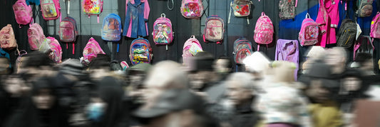 Rows of colourful school backpacks displayed above a busy shop floor
