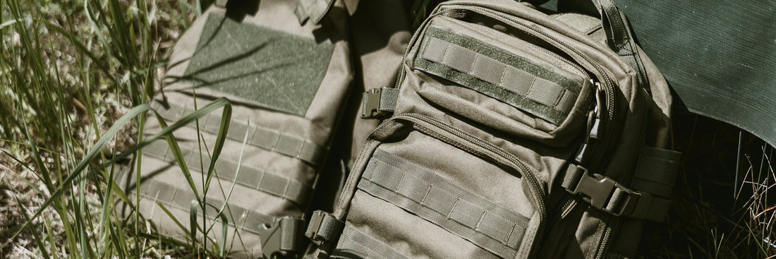 Tactical backpack and utility vest resting against a camouflage tarpaulin