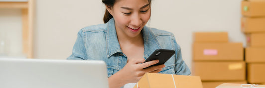 Seller checking a package against an order on a laptop, surrounded by boxes